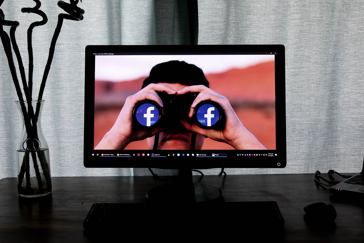 A monitor shows a man looking through binoculars with the Facebook logo
