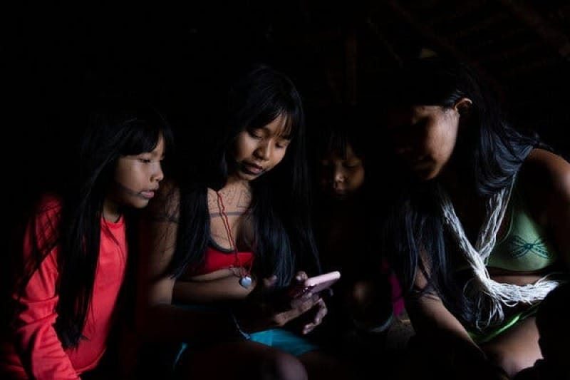 Four girls looking at the screen of a phone with a pink exterior.